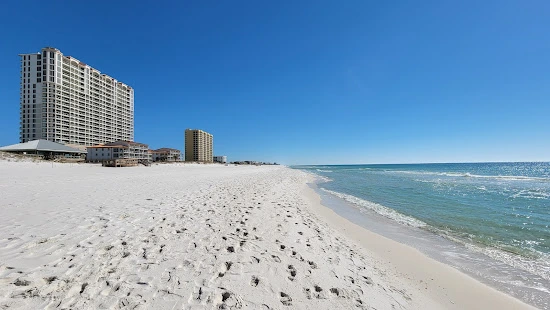 A sandy beach with buildings in the background, along with an ocean view taking place in Escambia County, Alabama.